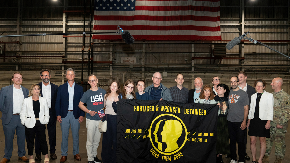 TOPSHOT - Former prisoners released by Russia, US journalist Evan Gershkovich (10thL), former US marine Paul Whelan (9thL), and US-Russian journalist Alsu Kurmasheva (8thL) pose behind a banner reading "Hostages and Wrongful Detainees, Bring Them Home" after landing at Joint Base San Antonio-Kelly Field, Texas, on August 2, 2024.