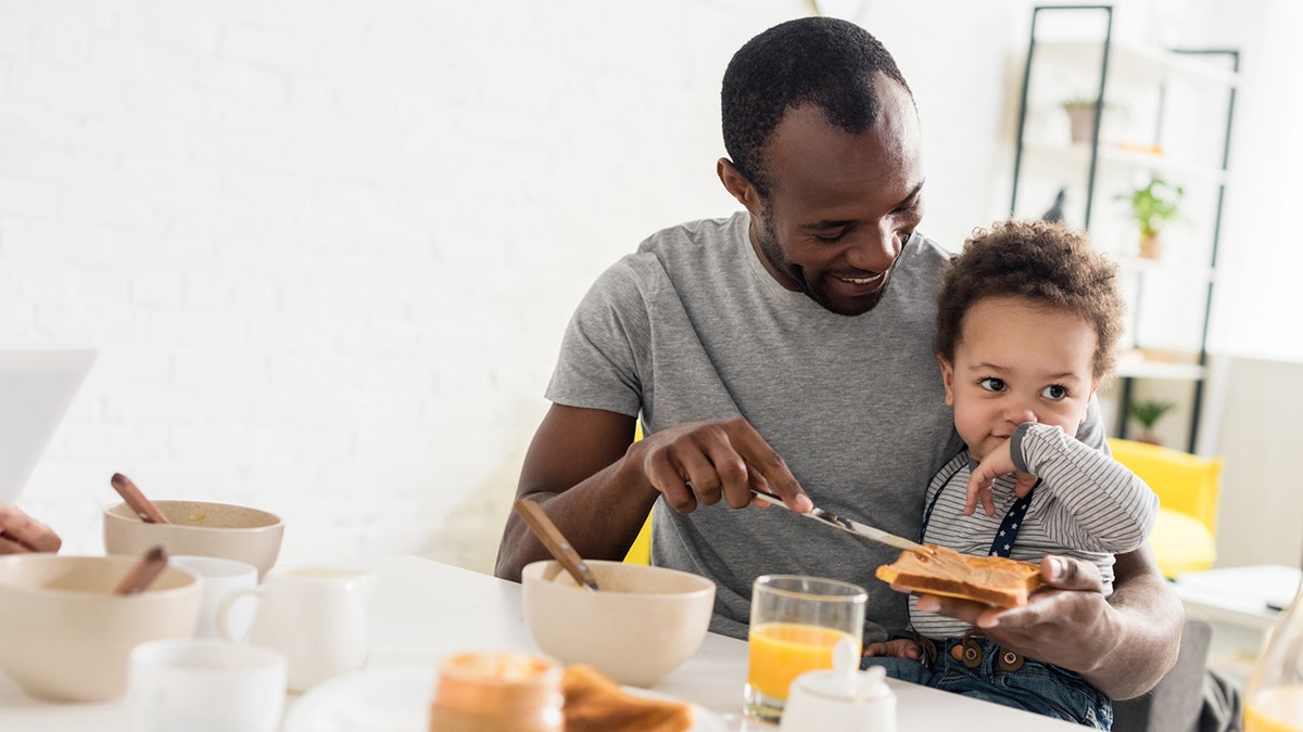 Father spreads peanut butter on his little son's toast