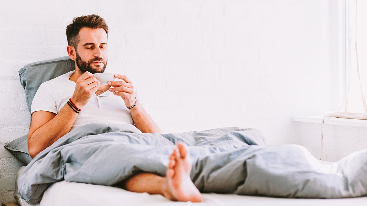 Joven bebiendo café en la cama