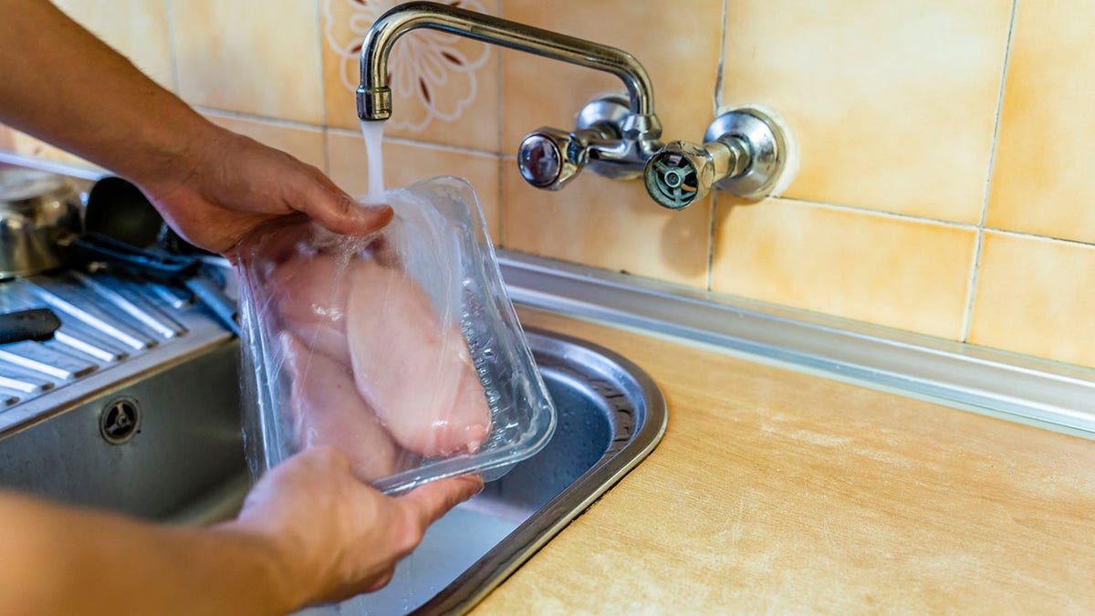 Person washing chicken in a package. This is dangerous.