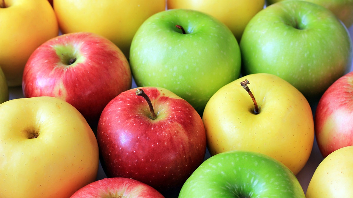 Manzanas rojas, amarillas y verdes sobre fondo oscuro.