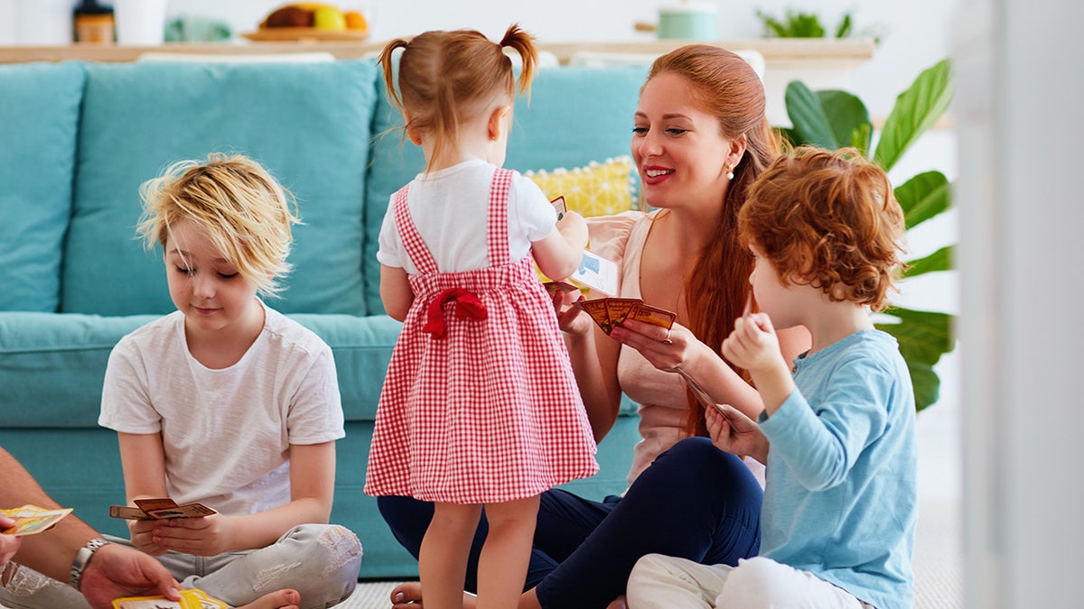 A happy family playing cards together on the floor at home. A woman and three children. All of them have red hair.