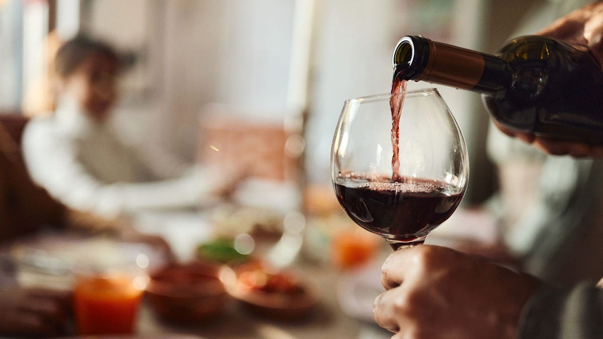 Close-up of a man pouring red wine into a glass in the dining room.