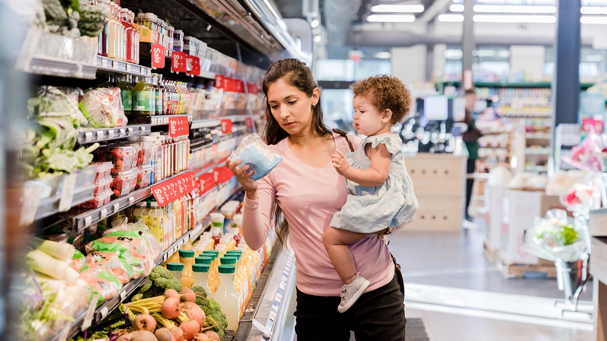 young mother holds daughter on her hip as she shops