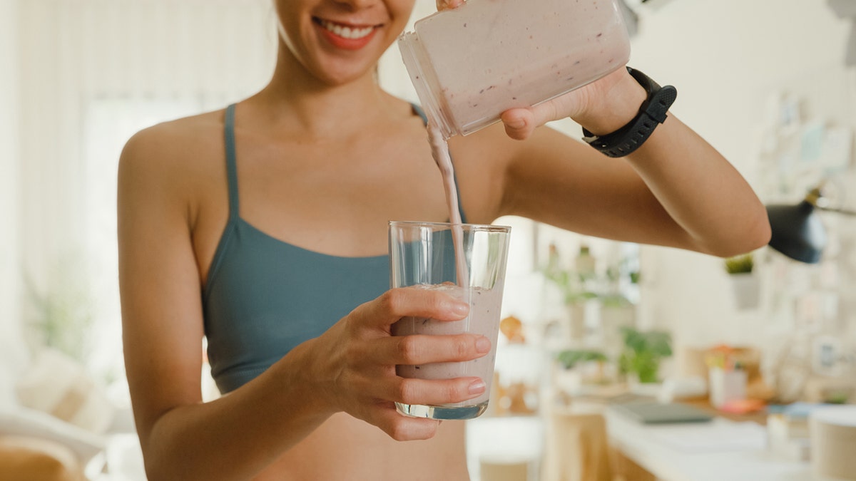 Woman pouring smoothie into glass using blender at home