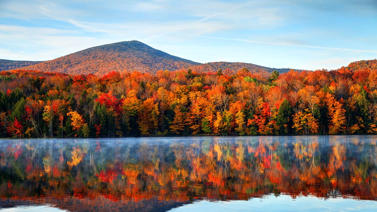 Luz de otoño a primera hora de la mañana cerca de Killington, Vermont, mostrando muchos árboles de distintos colores que se reflejan en el lago.