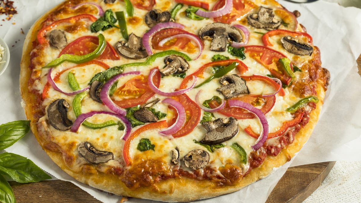 A photo of a homemade vegetarian pizza with mushrooms, peppers, tomatoes and spinach.