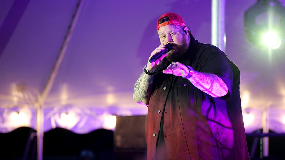 Country singer Jelly Roll wears a backwards red hat on stage.