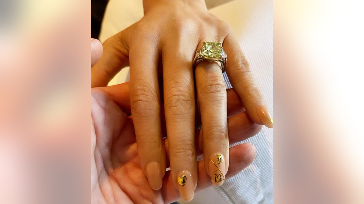 A photo of Jennifer Lopez's hand with her green diamond engagement ring and the letters 