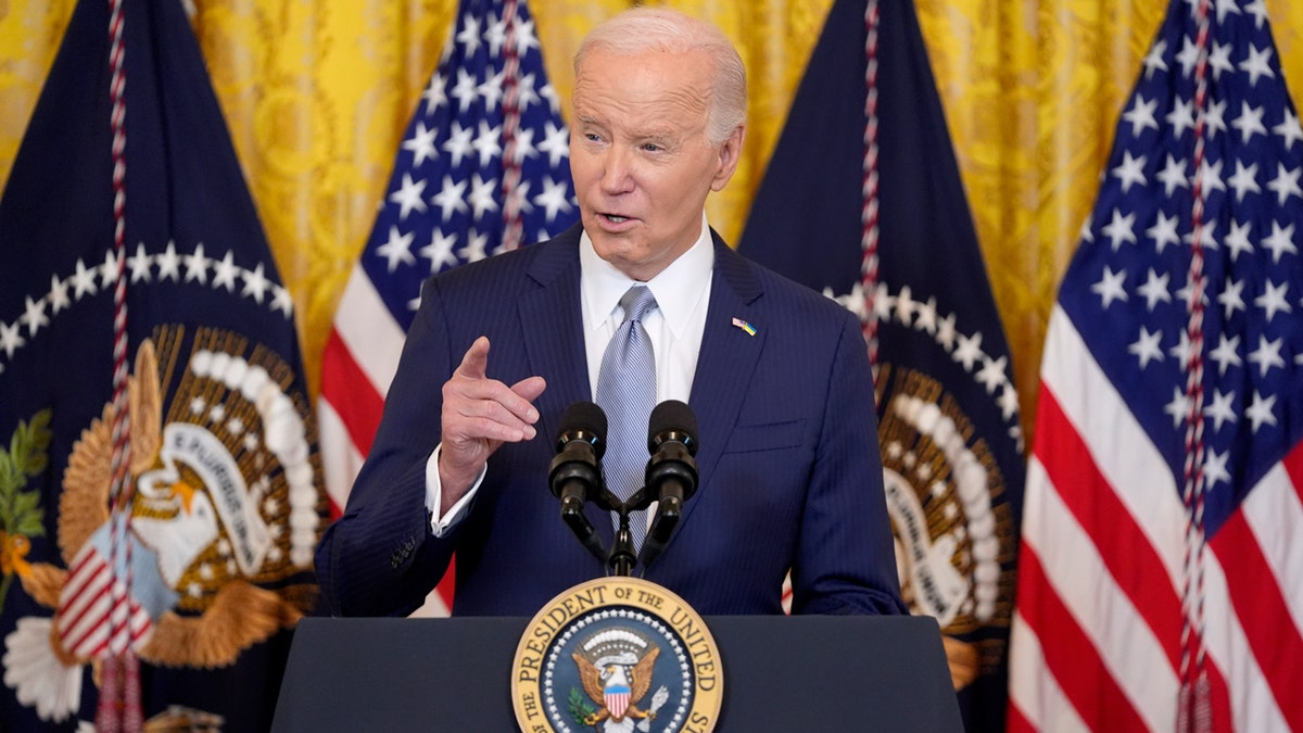 Joe Biden at lectern with US, presidential flags behind him