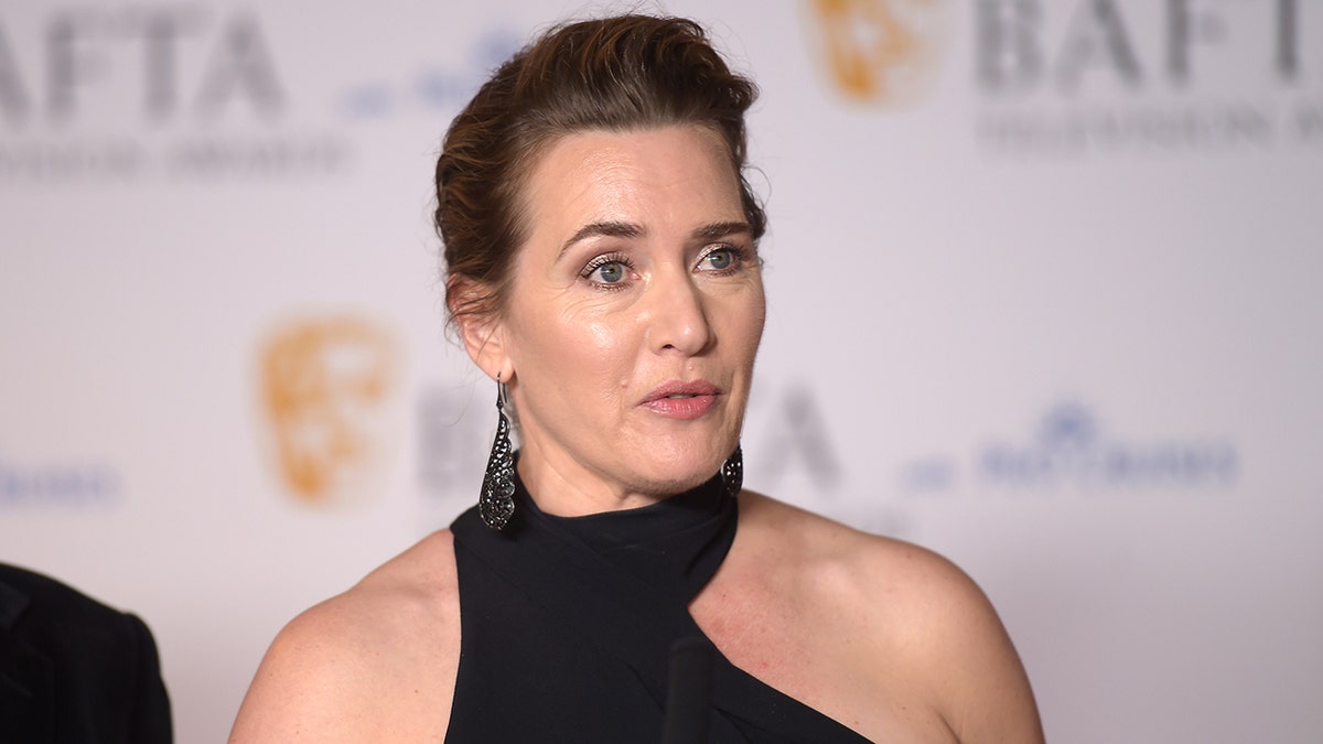 Kate Winslet dalam gaun halter asimetris di karpet tampak berbicara