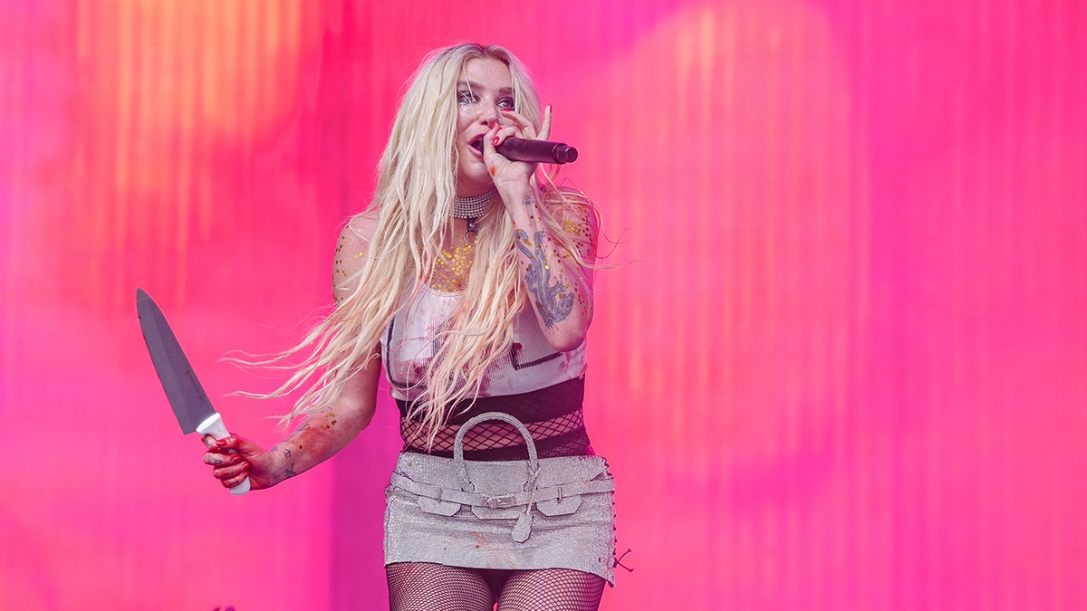 Kesha holds a knife in her right hand at Lollapalooza and sings into the microphone with her left hand