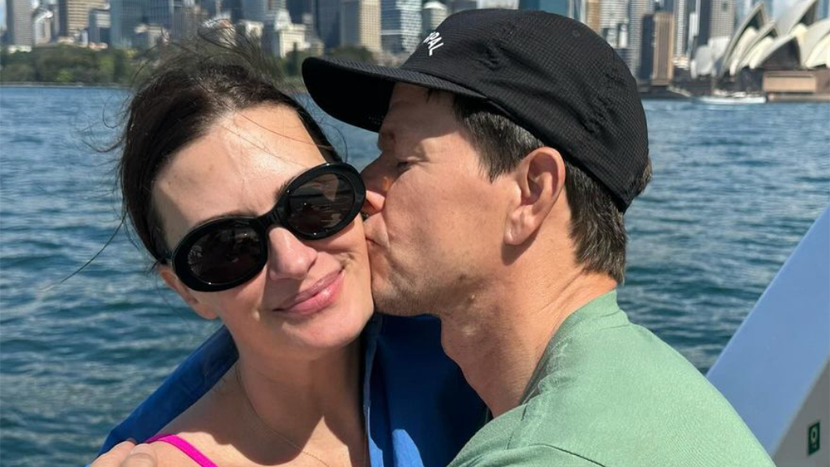 Mark Wahlberg con camisa verde y sombrero negro le da un beso en la mejilla a su mujer Rhea