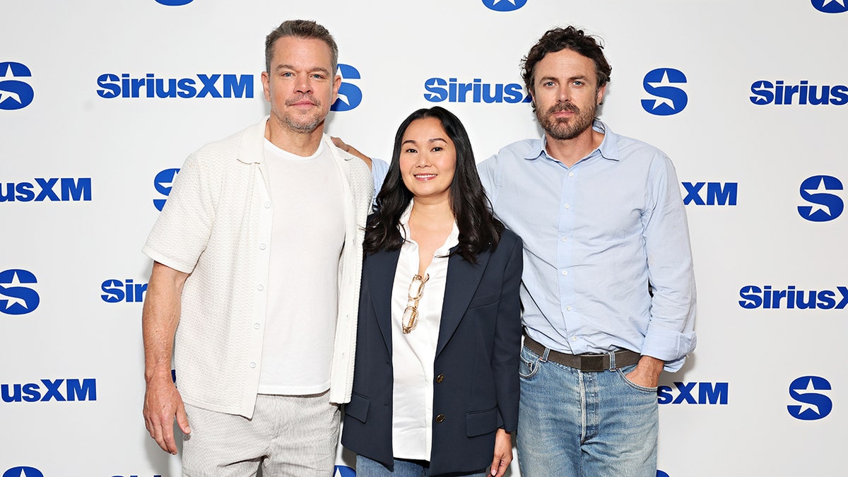 Matt Damon in a white shirt soft smiles with co-stars Hong Chau, in a navy blazer and Casey Affleck, in a light blue shirt