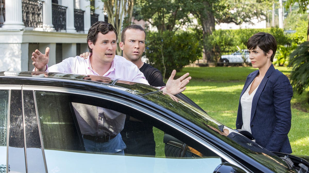 Gabriel Olds in a pink shirt being pushed against a car from an episode of NCIS: New Orleans