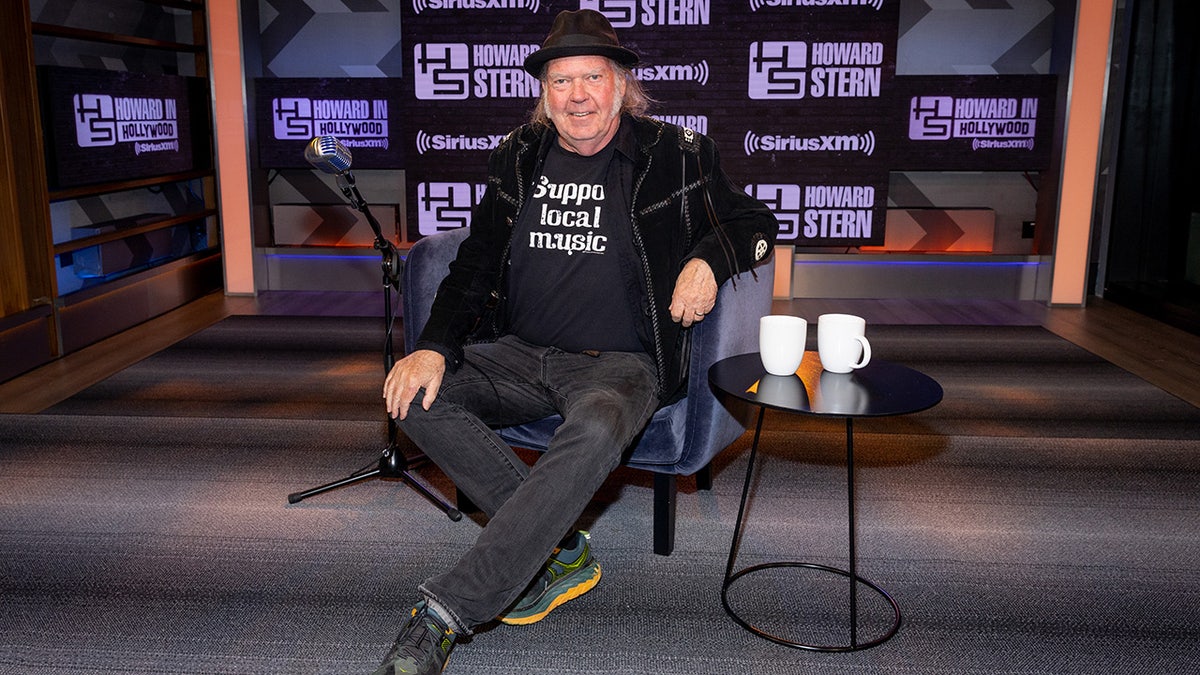 Neil Young smiles while sitting in a chair