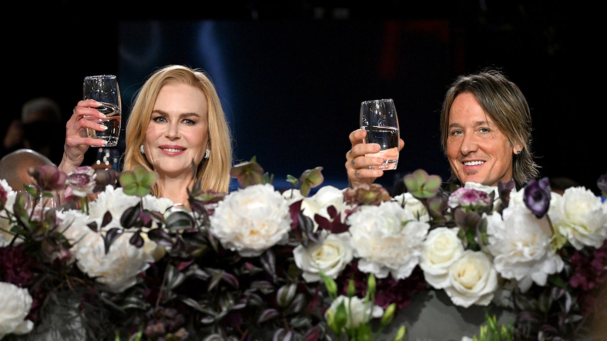 Nicole Kidman and Keith Urban behind a floral arrangement both lift their glasses