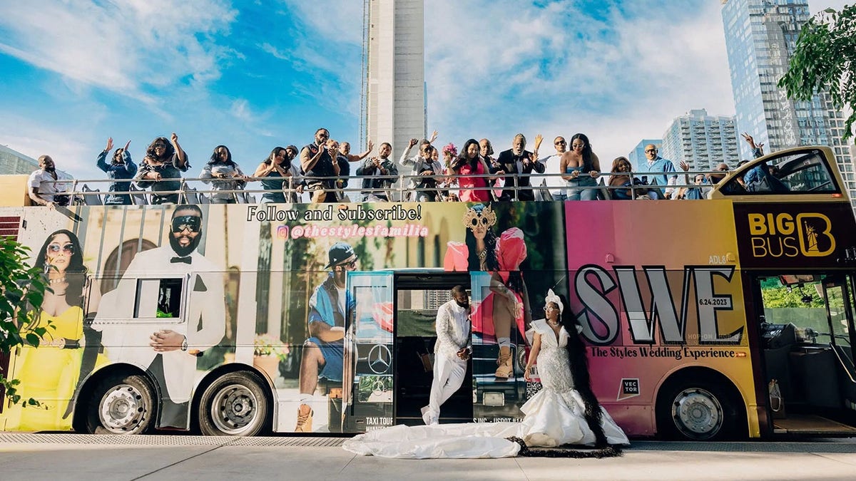 Los invitados a la boda y los novios posan delante de un autobús turístico personalizado.