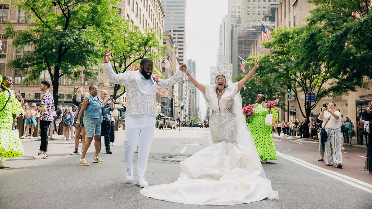 Novios celebrando en la calle con las manos sobre la cabeza.