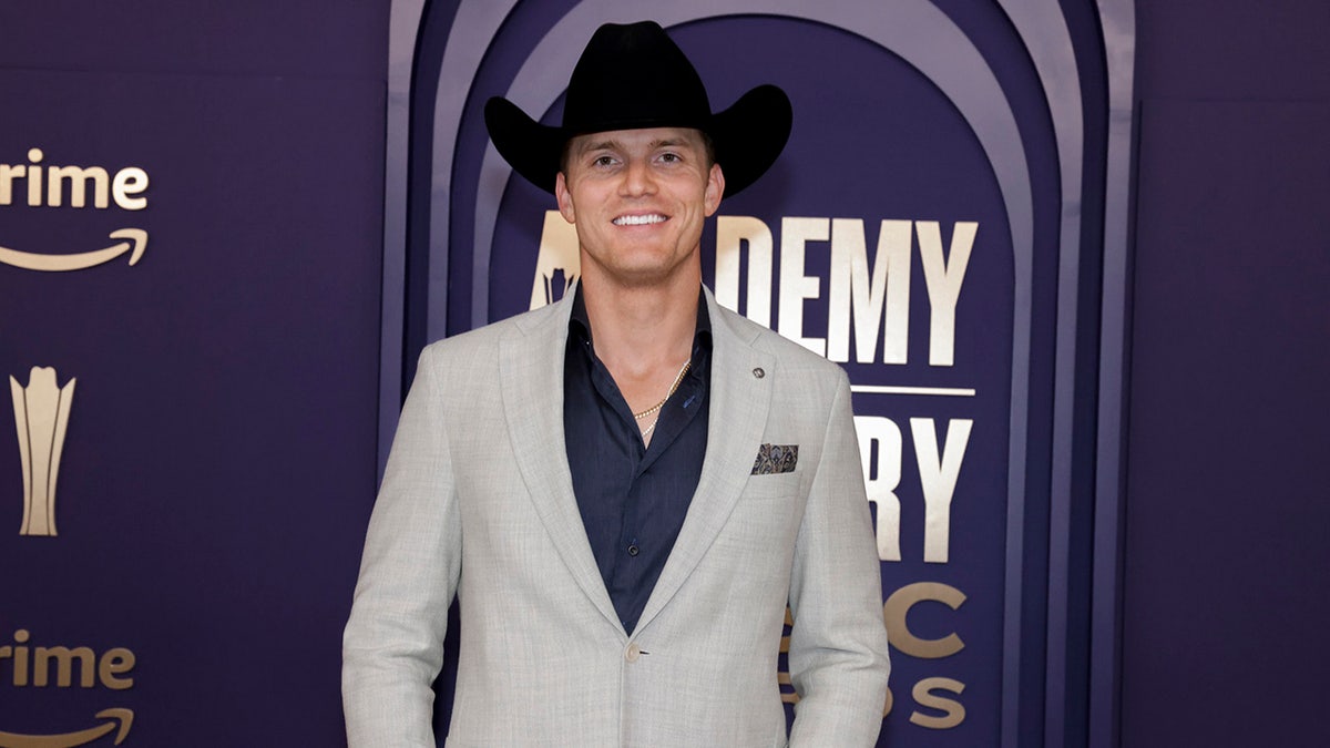 Parker McCollum in a navy shirt, grey suit and black cowboy hat at the CMAs