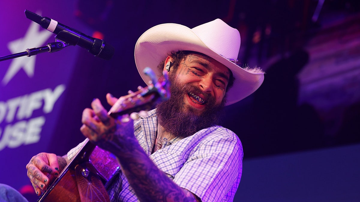 Musician Post Malone wears a cowboy hat while playing guitar.