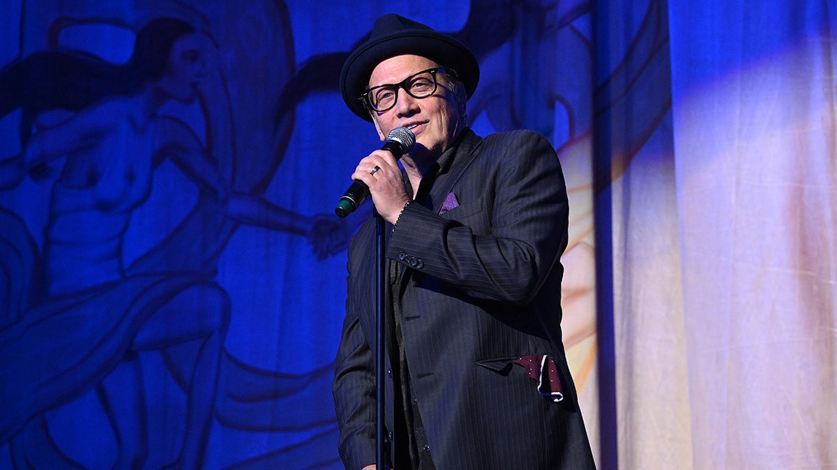 Rob Schneider con sombrero de copa y traje azul marino actúa en el escenario