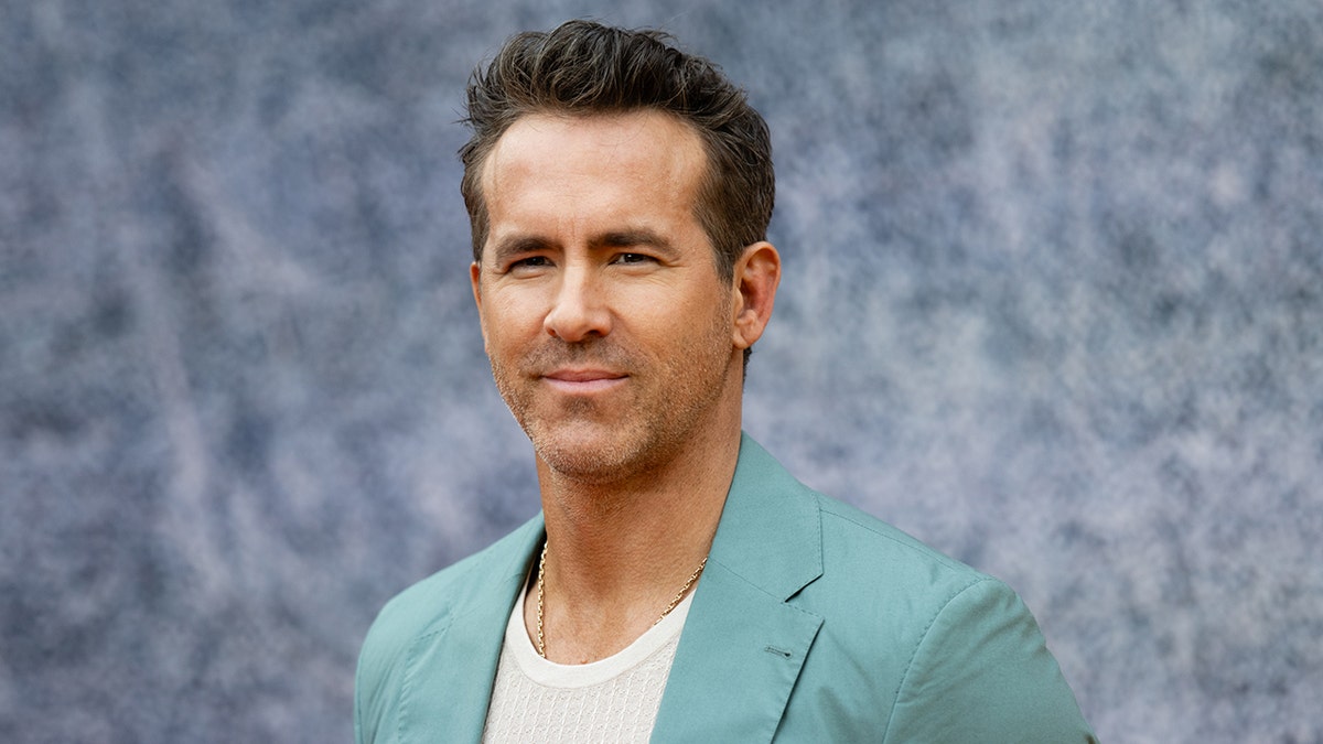 Ryan Reynolds con un blazer turquesa sonríe suavemente en la alfombra