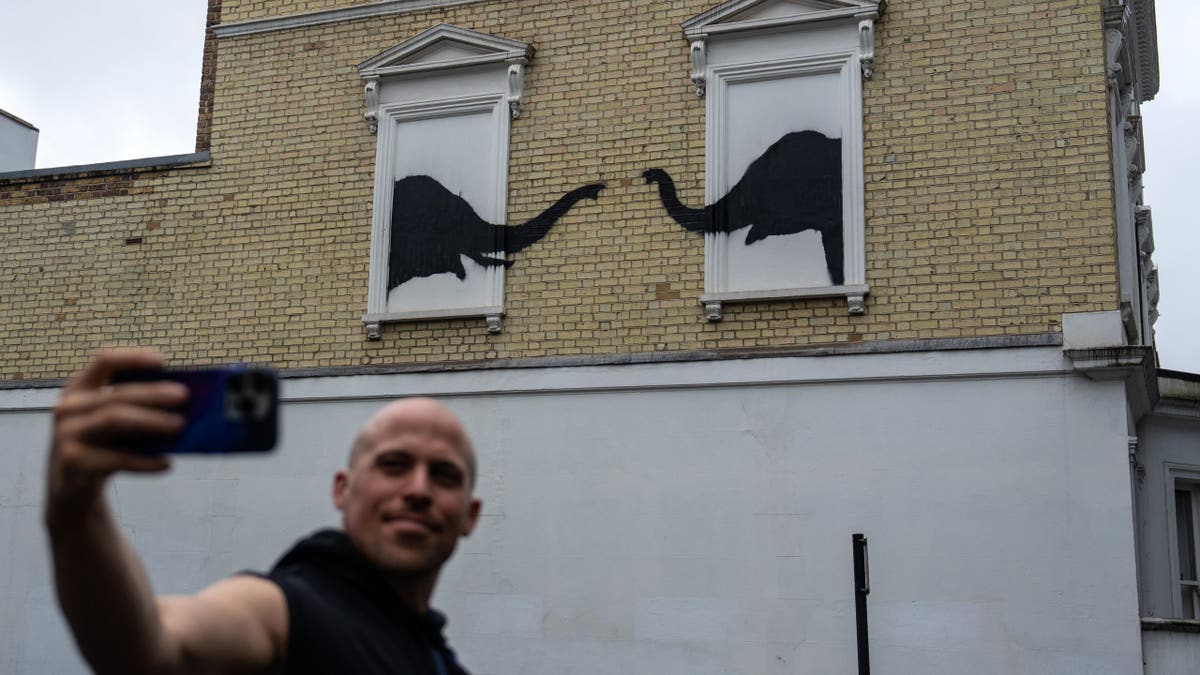 Hombre tomándose un selfie delante de una obra de Banksy