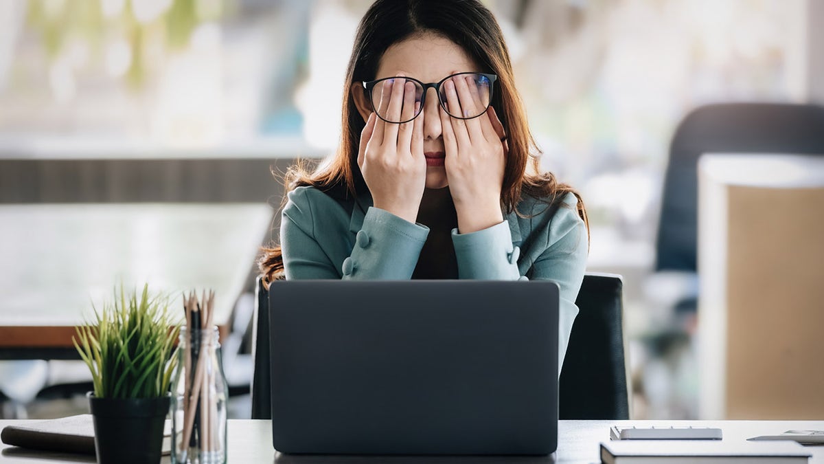 Mujer frotándose los ojos en el trabajo.