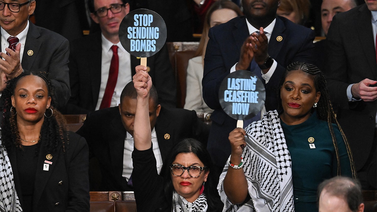 Las Rep. Rashida Tlaib y Cori Bush sostienen carteles de protesta durante el discurso del Presidente Biden sobre el Estado de la Unión