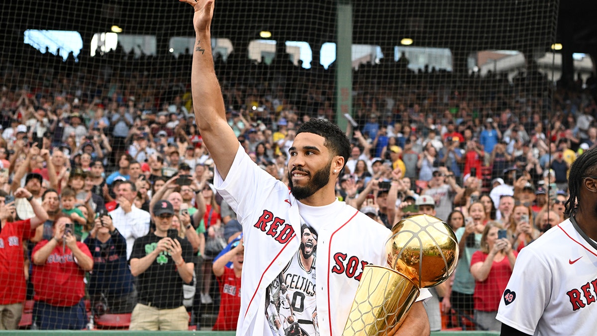 Jayson Tatum sostiene un trofeo de la NBA en un partido de los Red Sox