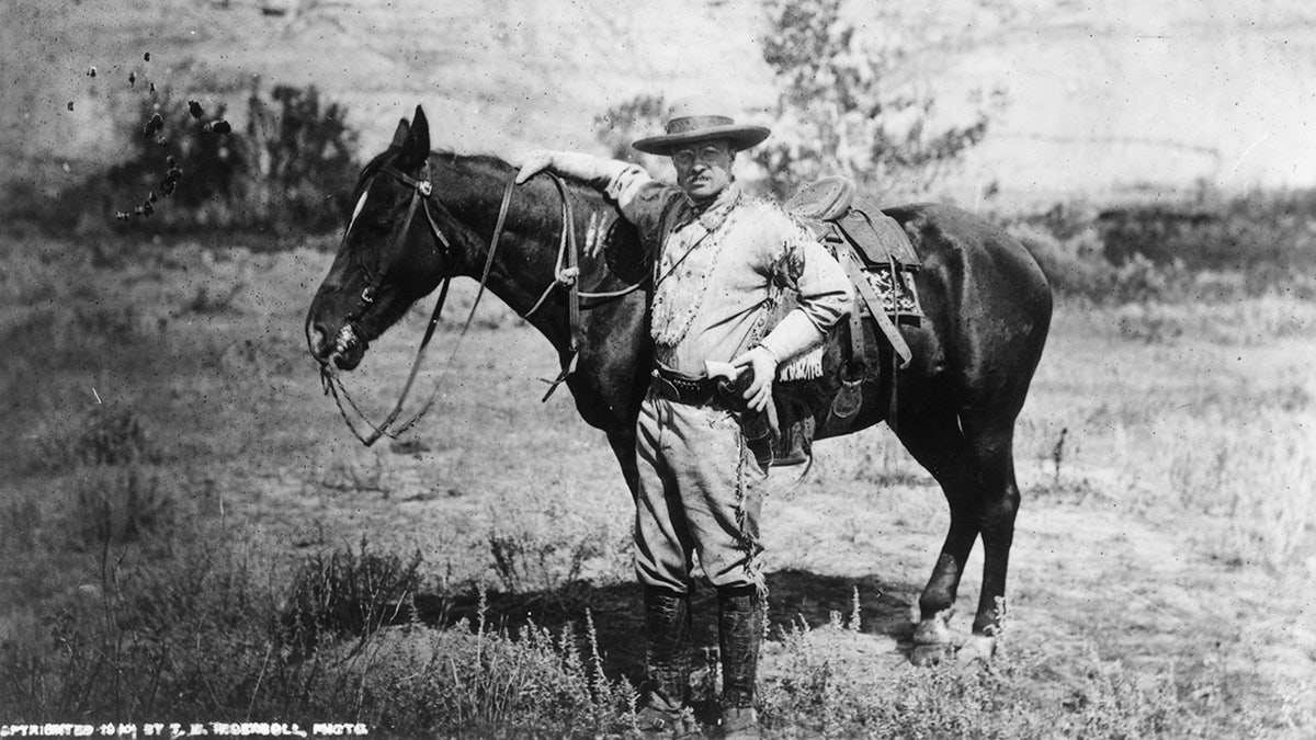 Theodore Roosevelt stands next to horse