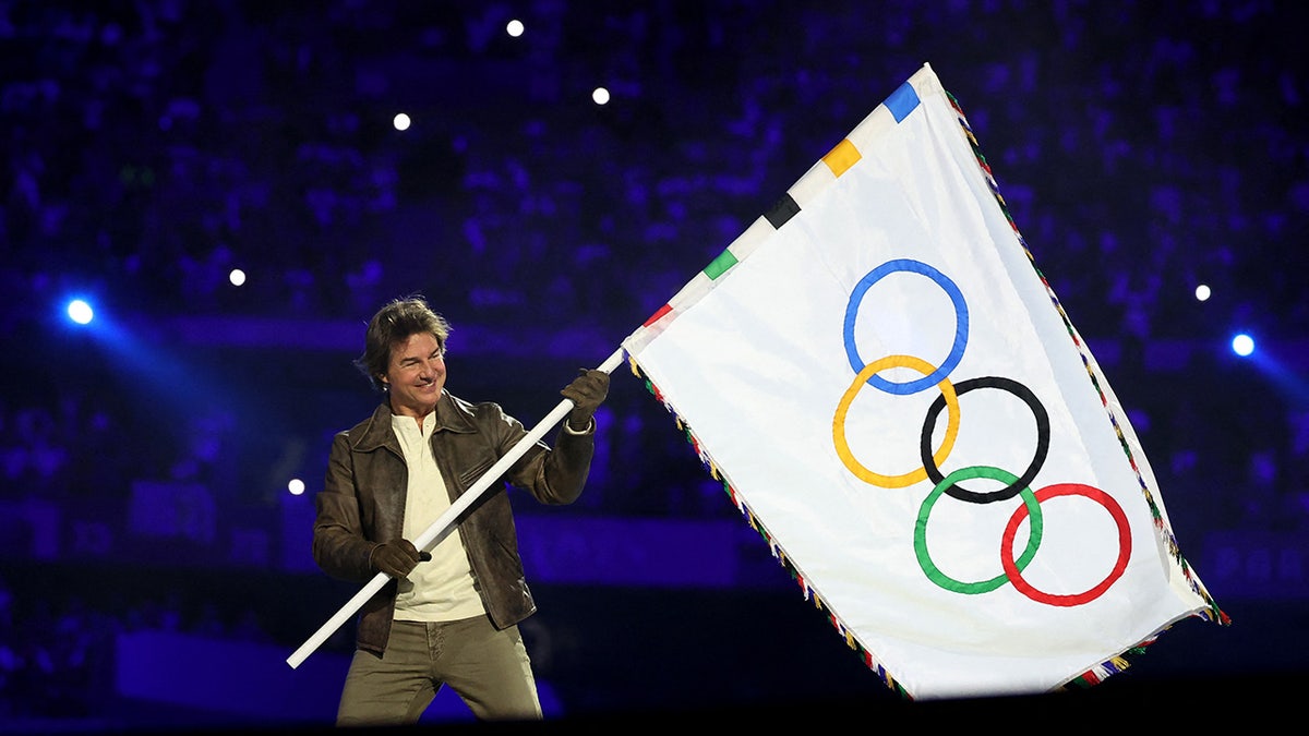 O ator Tom Cruise segura a bandeira das Olimpíadas durante a cerimônia de encerramento.