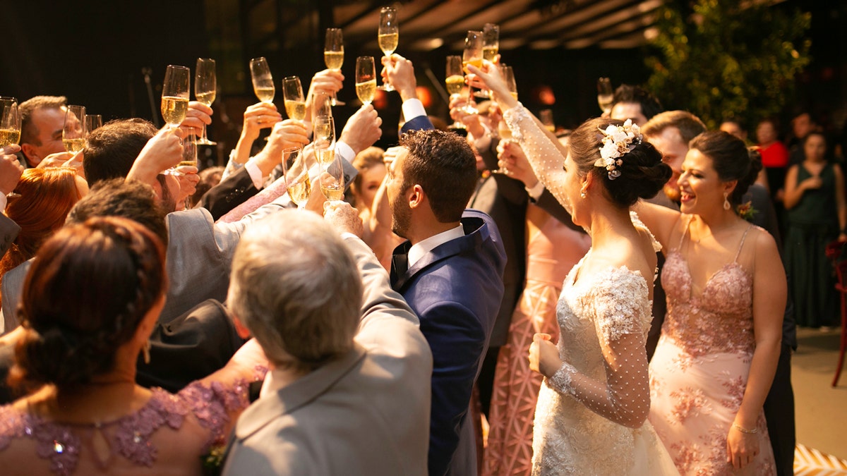 A bride and groom celebrate with guests during a toast at their wedding reception.