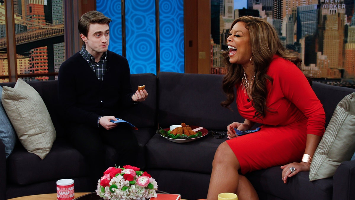 Wendy Williams laughs in a red dress on her couch with guest Daniel Radcliffe