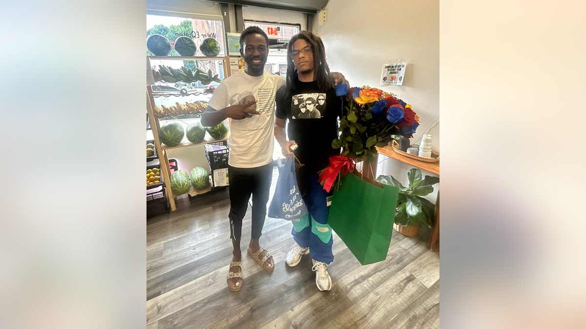 Wendy Williams son Kevin Hunter Jr. smiles holding a green shopping bag and flowers with the owner of the African Bio Mineral Cell Food store