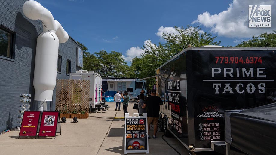 A taco truck, portable toilets and an abortion van parked beside a buiding