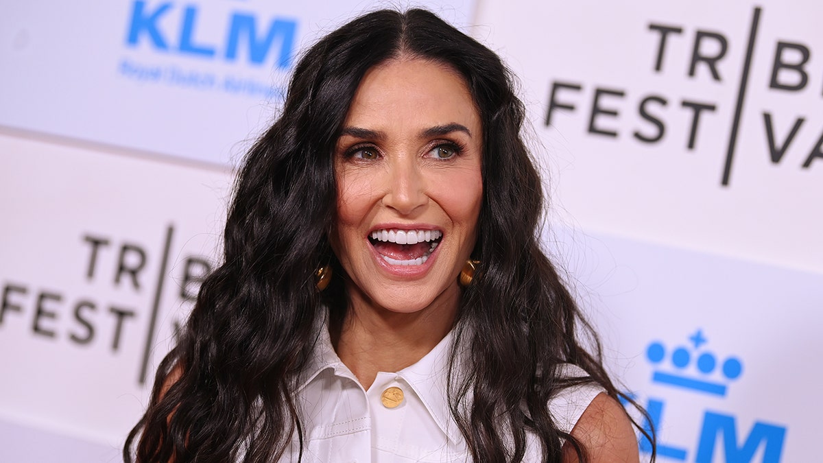 Demi Moore smiles broadly on the carpet in a white sleeveless top