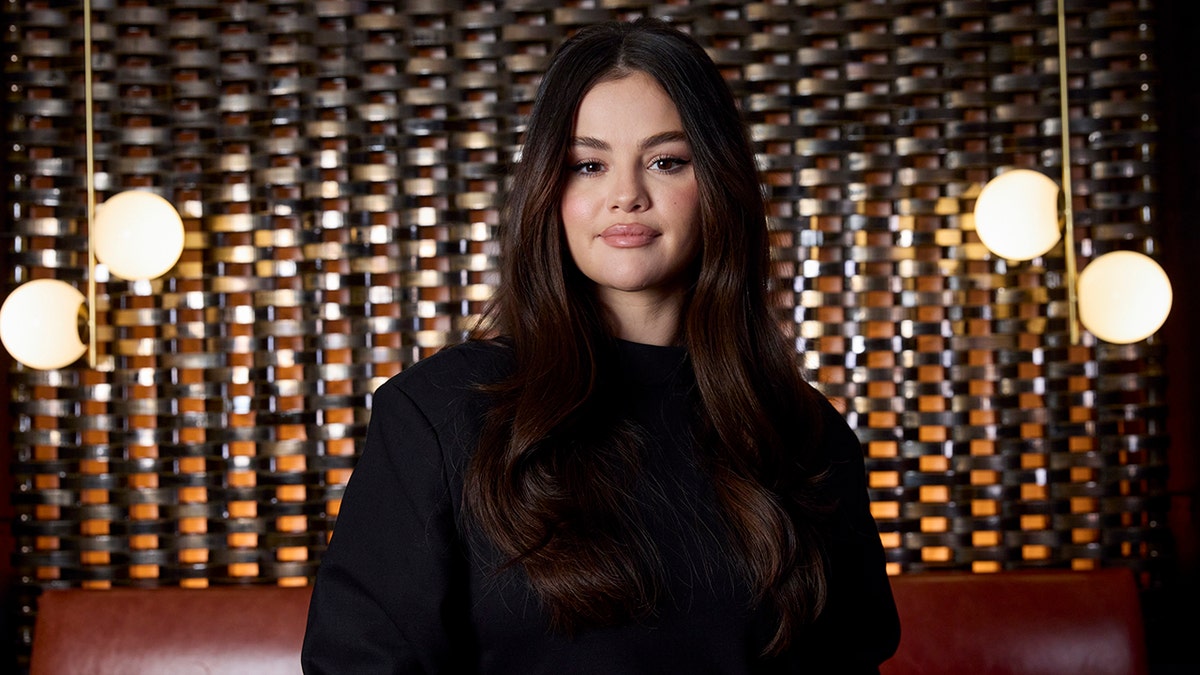 Selena Gomez in a black dress looking straight into the camera with lights behind her