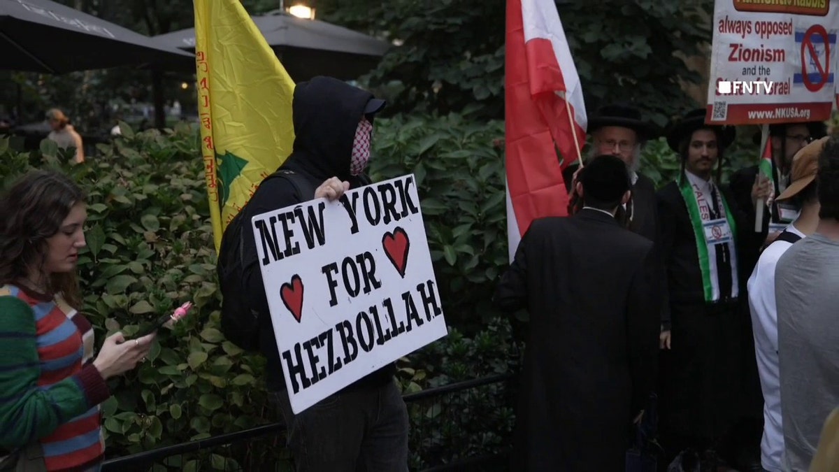 Manifestante anti-Israel sosteniendo un cartel y una bandera de Hezbolá