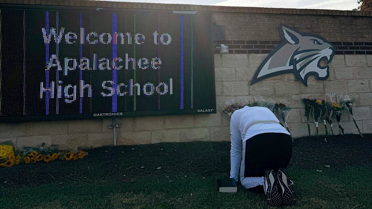 A person kneels in front of flowers that are placed outside the entrance to Apalachee High School