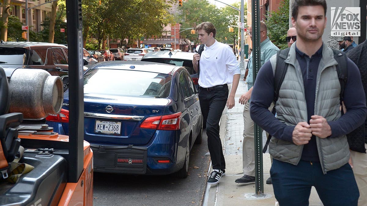 Barron Trump wears a white polo shirt, black jeans and Adidas sneakers as he leaves college with a black backpack on his shoulder