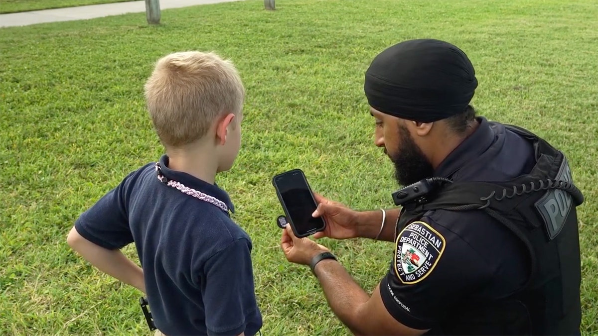 Un niño y un agente examinan una moneda con código QR utilizando un smartphone