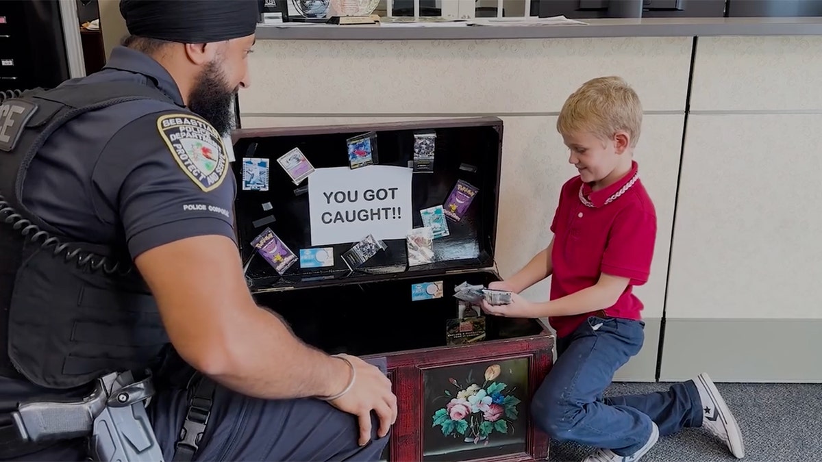 An officer and a child look through a treasure chest labeled 