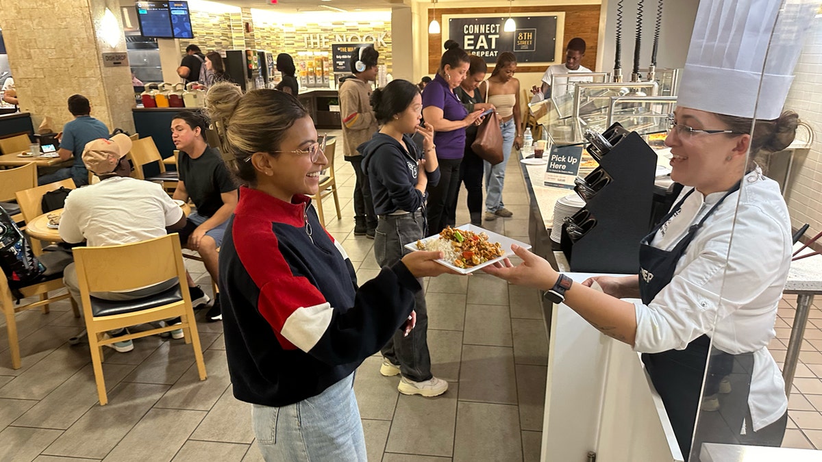 FIU pupil  Jocelyn Hernandez receives the nutrient  she ordered utilizing the Beastro kiosk from cook  Denisse Castillo.