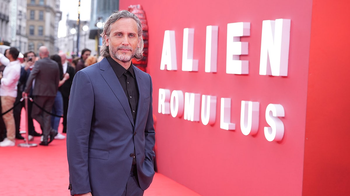 Fede Alvarez posing next to the Alien: Romulus poster on the red carpet