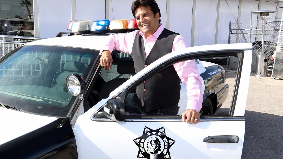 Erik Estrada posando com carro de polícia 