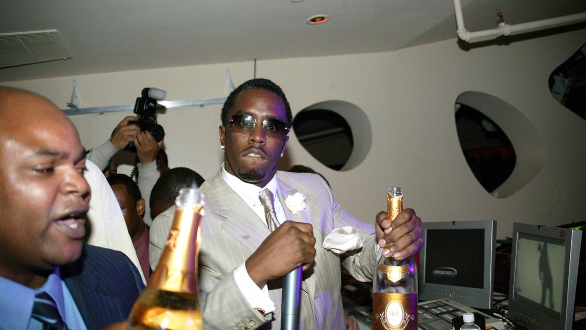 Sean Combs holds a microphone and a bottle of alcohol in his hand.