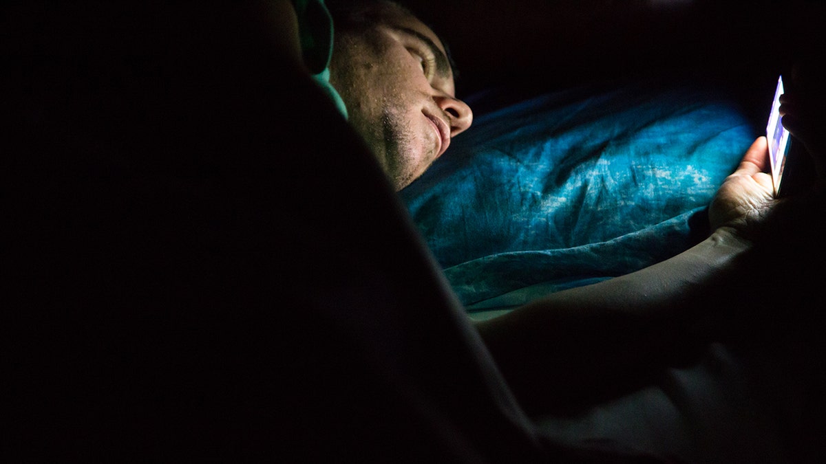 Hombre tumbado en la cama a altas horas de la noche en una habitación oscura consultando su smartphone.