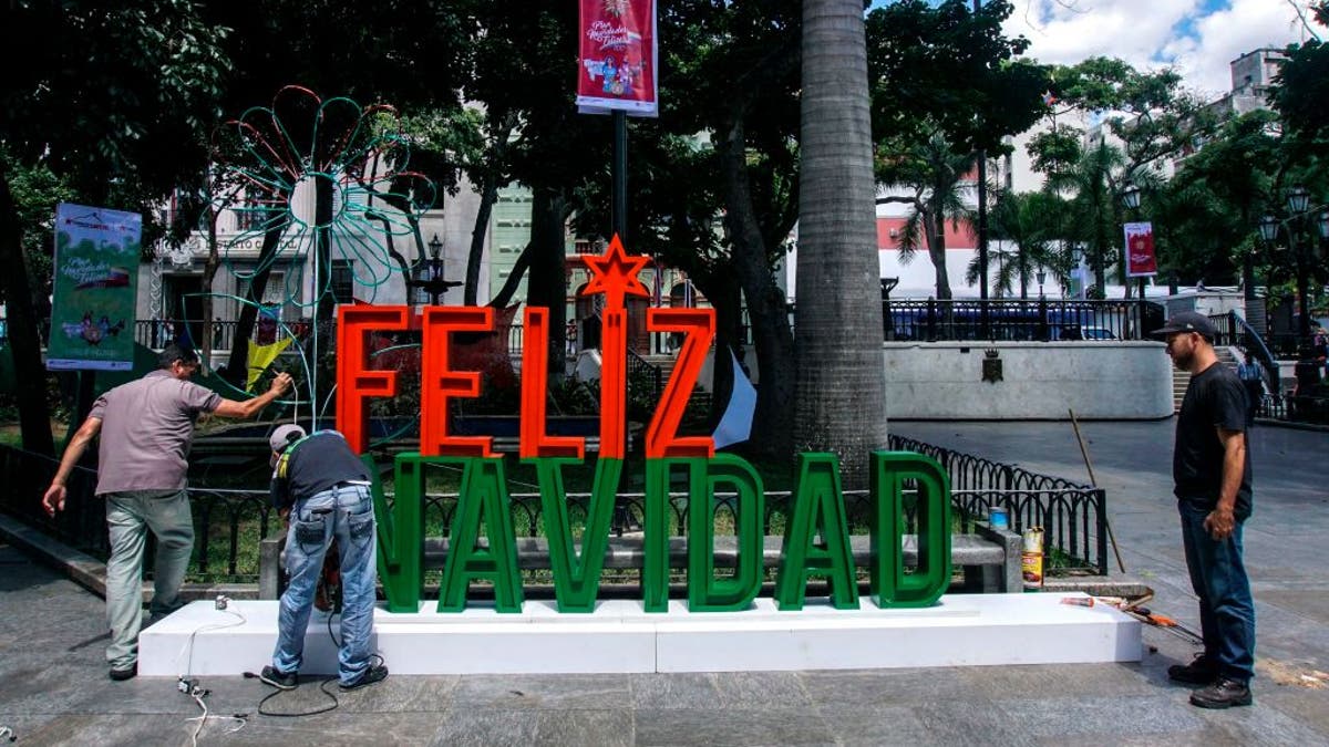 Men work on the installation of a christmas sign in Caracas on November 2, 2017.
